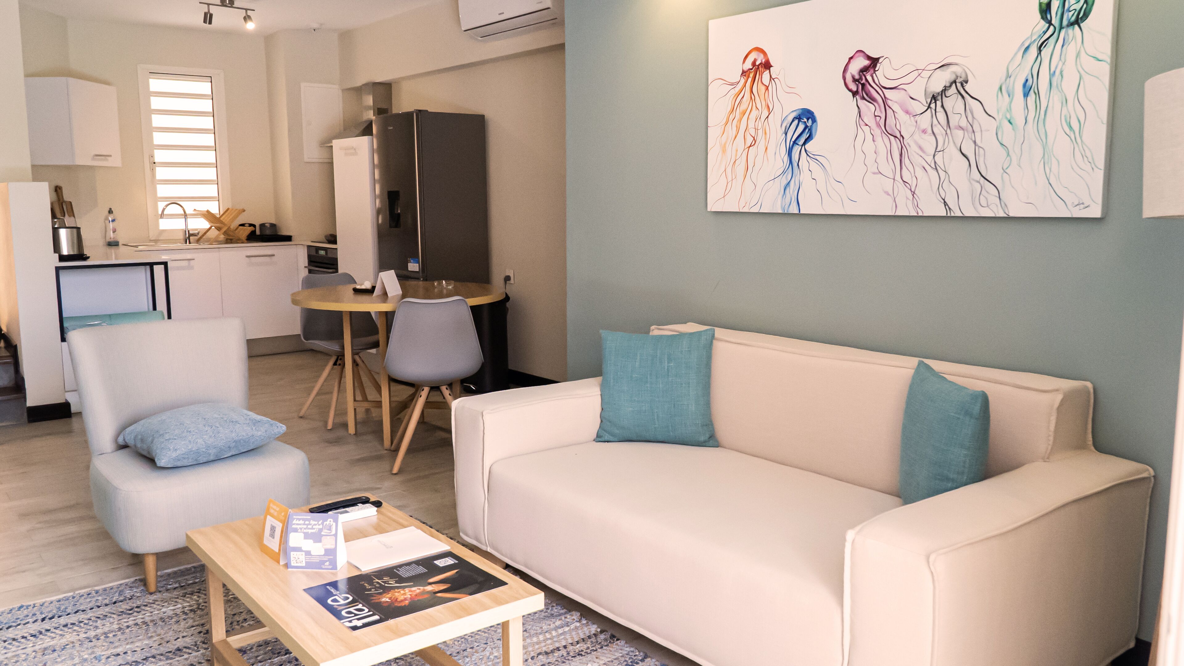 Una sala de estar moderna con un sofá blanco, dos sillones, una mesa de centro con revistas y un cuadro de medusas en la pared.