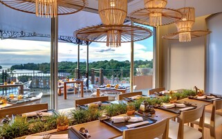 Un restaurante con terraza al aire libre y vistas panorámicas a un lago y vegetación.