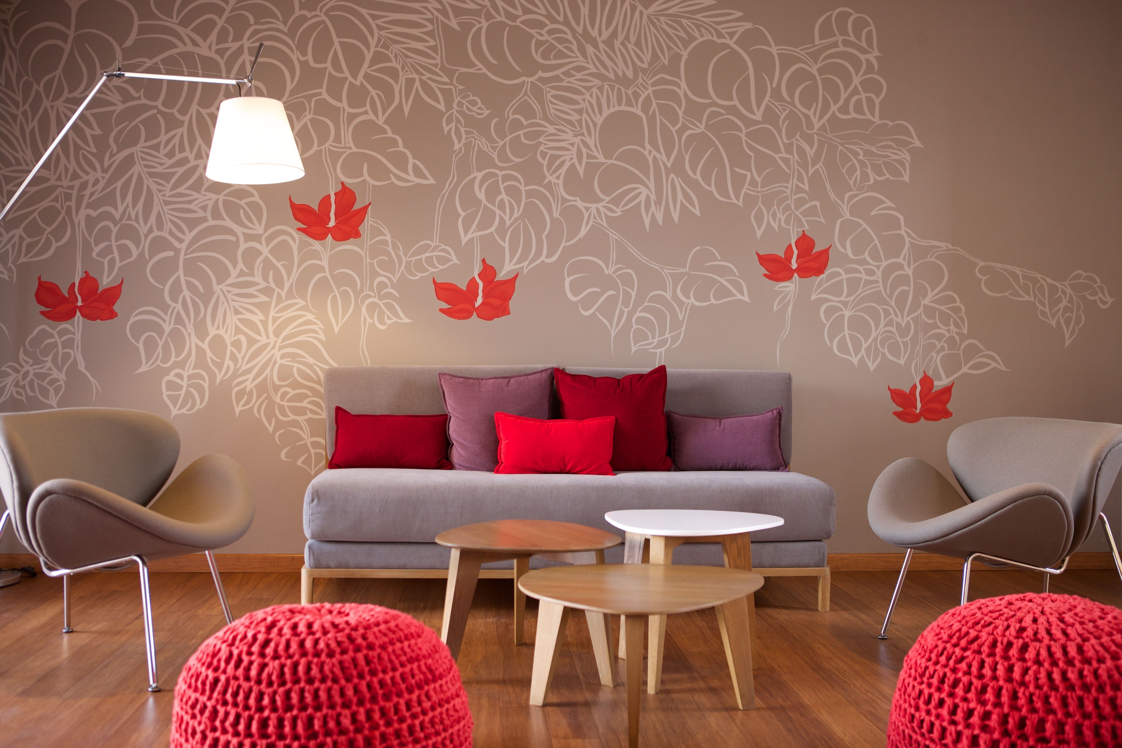 A modern living room with a grey sofa, red cushions, two grey armchairs, a wooden coffee table, and a floor lamp.