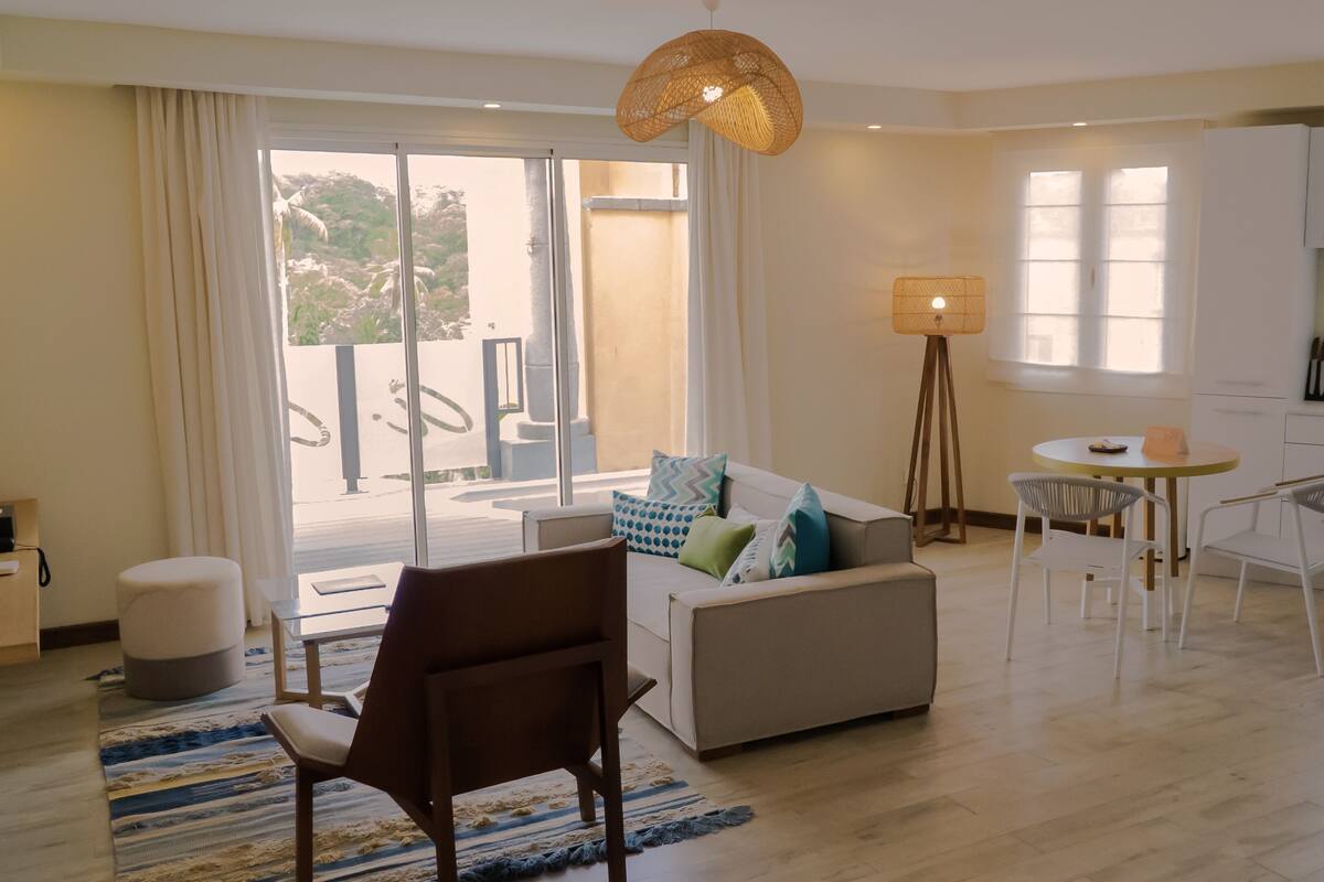 A modern living room with a sofa, chairs, a dining table, and a kitchen area.