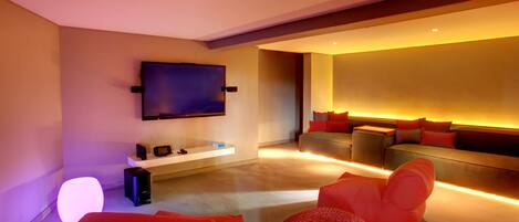 A modern living room with a flat-screen TV mounted on the wall, a sofa with red cushions, and a coffee table.