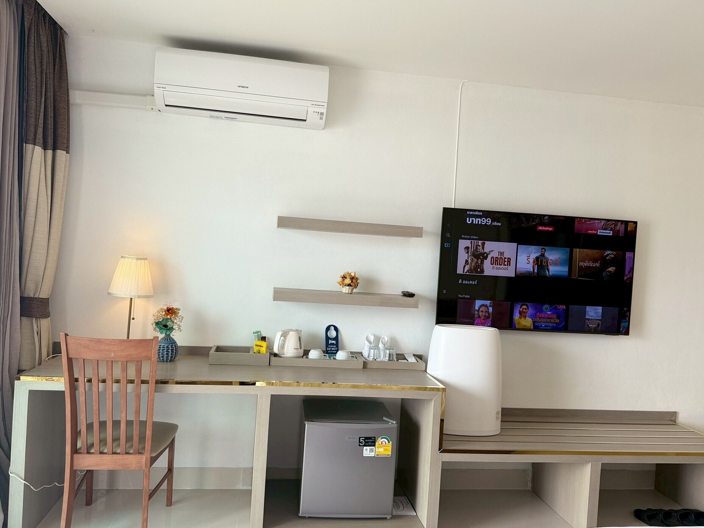 Habitación de hotel con escritorio, silla, aire acondicionado, televisión y un refrigerador pequeño.