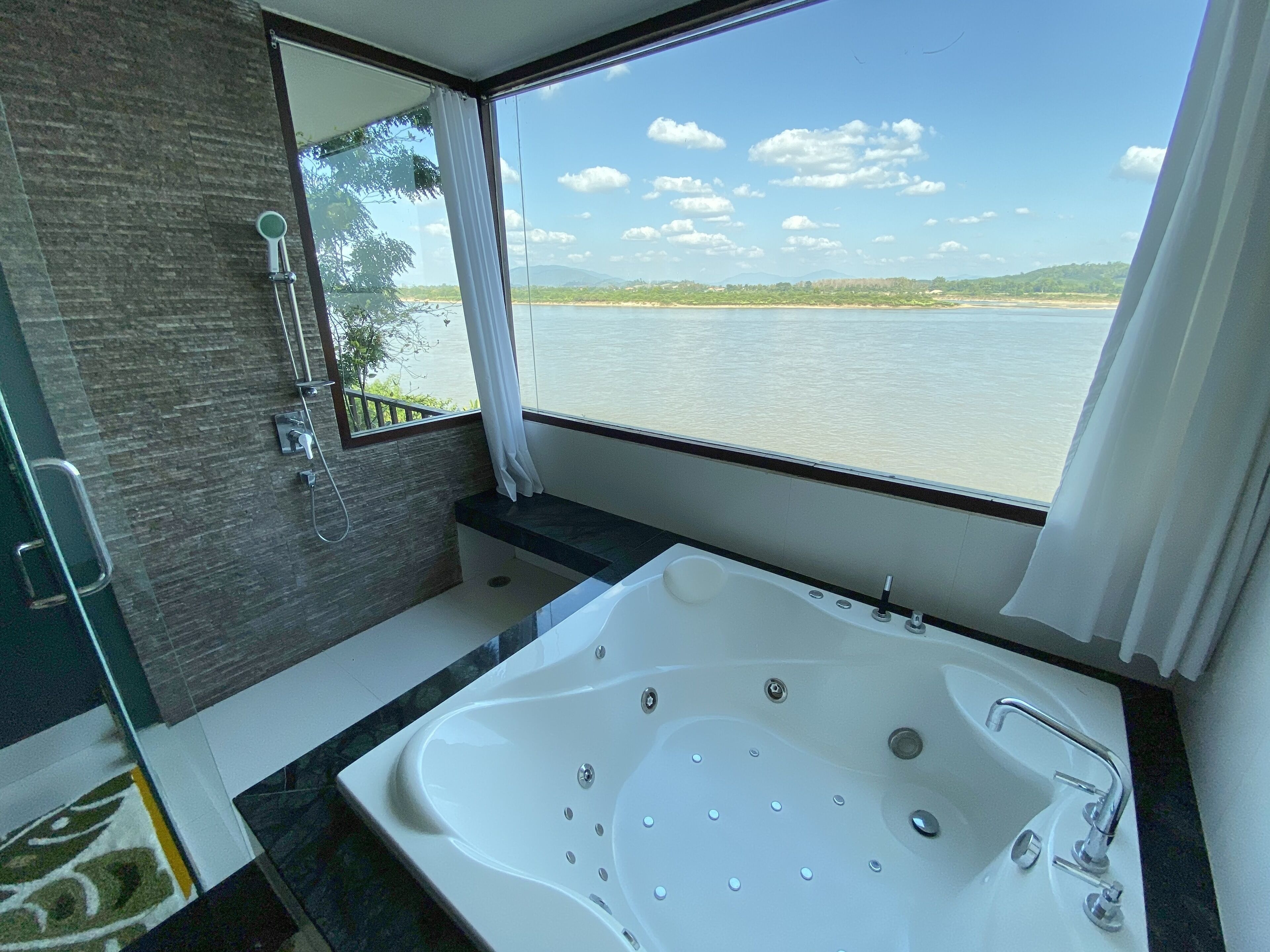 Un baño con una bañera grande, ducha y ventana con vistas al agua.