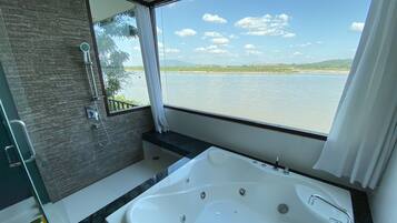 Un baño con una bañera grande, ducha y ventana con vistas al agua.
