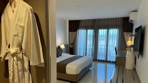 Una habitación de hotel con cama, escritorio, televisor y bata colgada en un perchero.