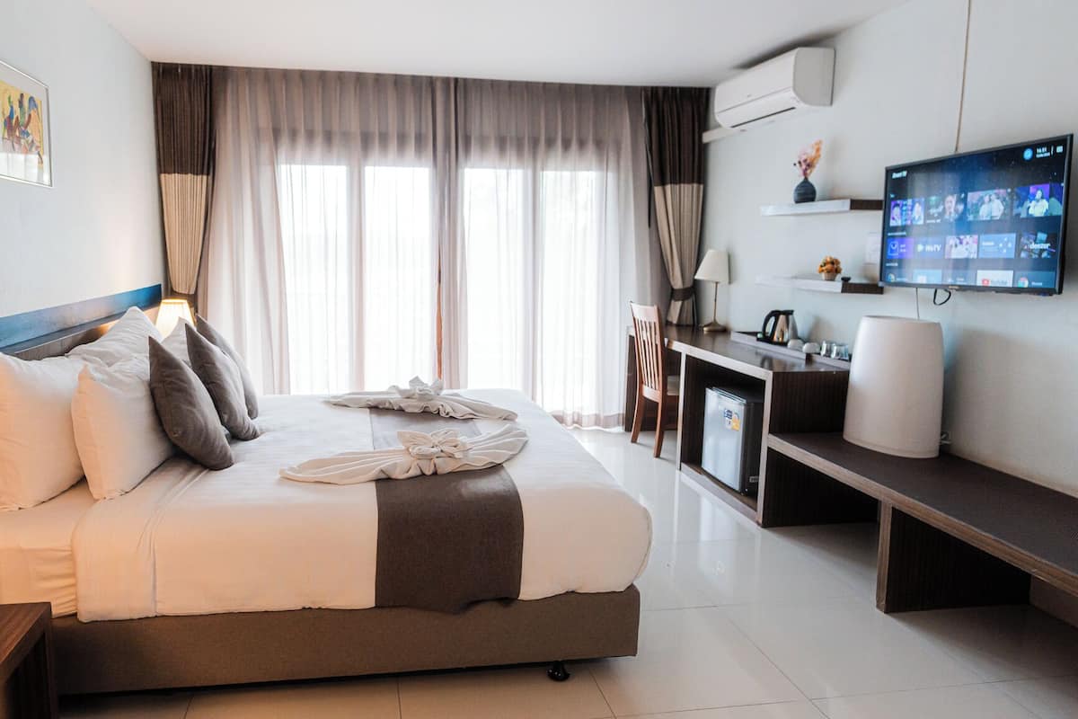 Habitación de hotel con cama, escritorio, televisor y ventana con cortinas.