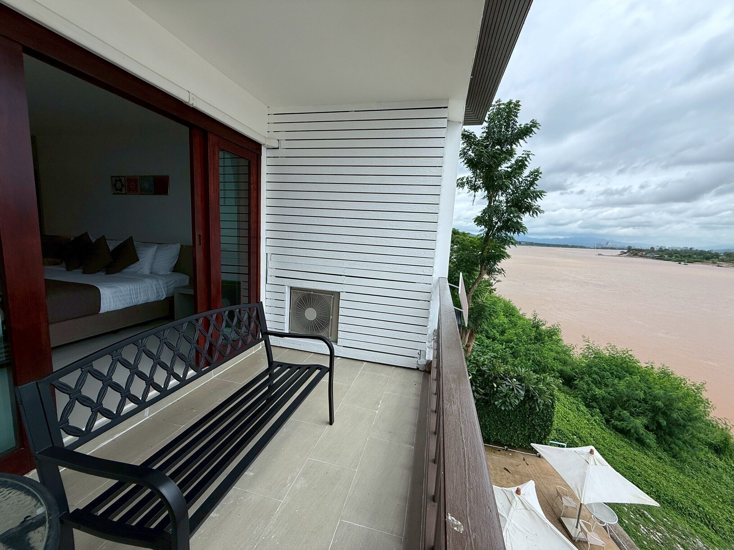 A balcony with a bed, a bench, and a view of a river.