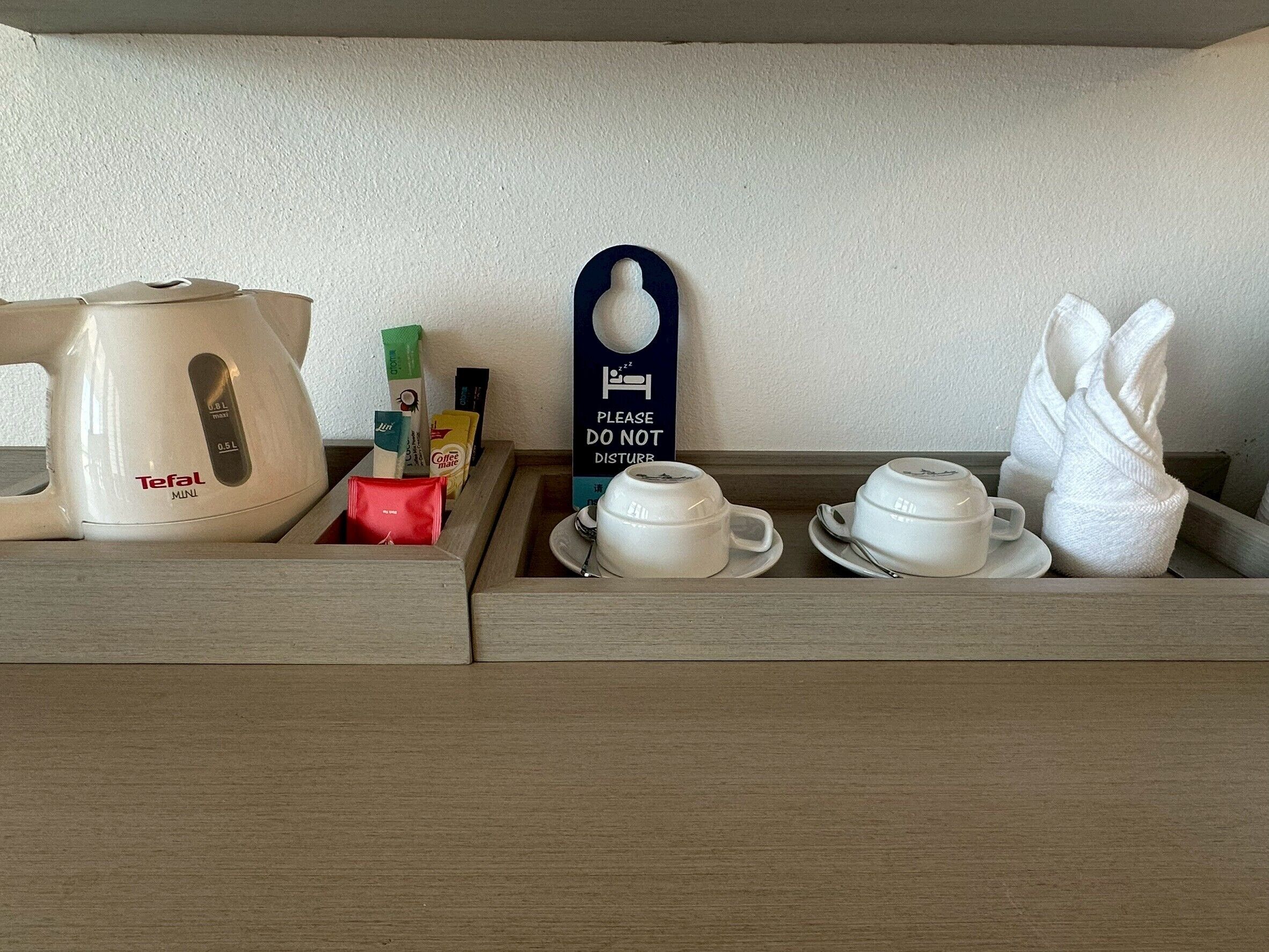 A drawer with a coffee maker, tea bags, a sign, and cups.