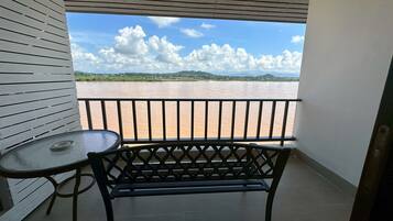 A balcony with a view of a river and distant hills, a black metal bench, and a small round table.