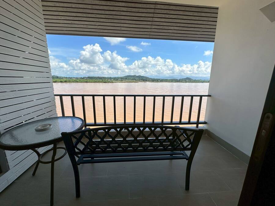 A balcony with a view of a river and distant hills, a black metal bench, and a small round table.
