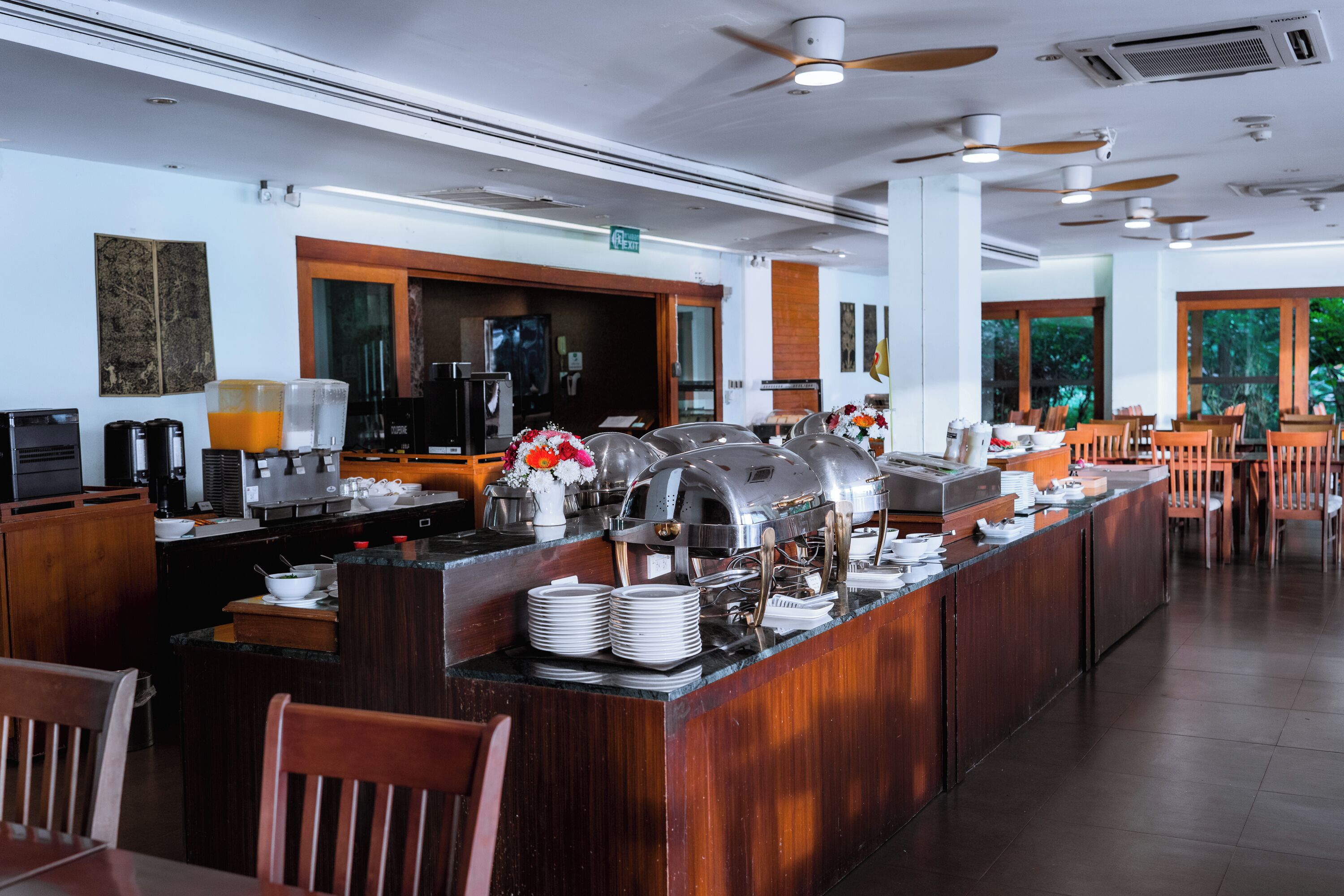 A buffet setup with a self-service station, a coffee machine, and a seating area with wooden chairs.
