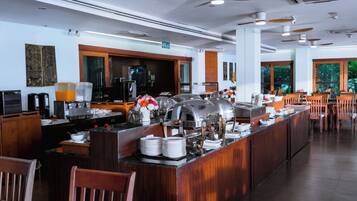 A buffet setup with a self-service station, a coffee machine, and a seating area with wooden chairs.