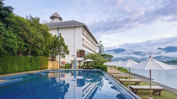 Una piscina con vistas a montañas, un edificio con balcones y sombrillas.