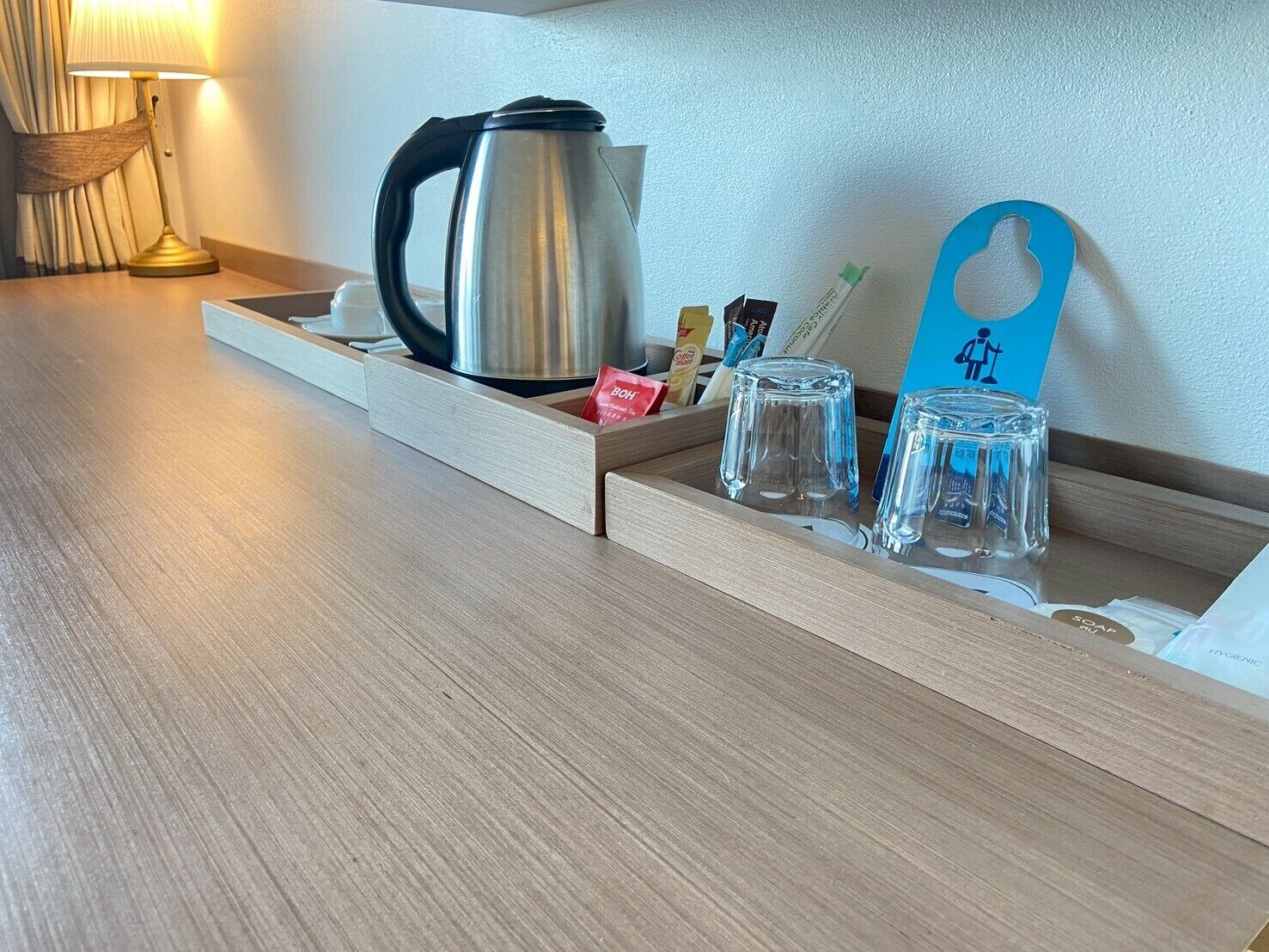 A wooden tray with a kettle, glasses, and a blue card with a toilet symbol.