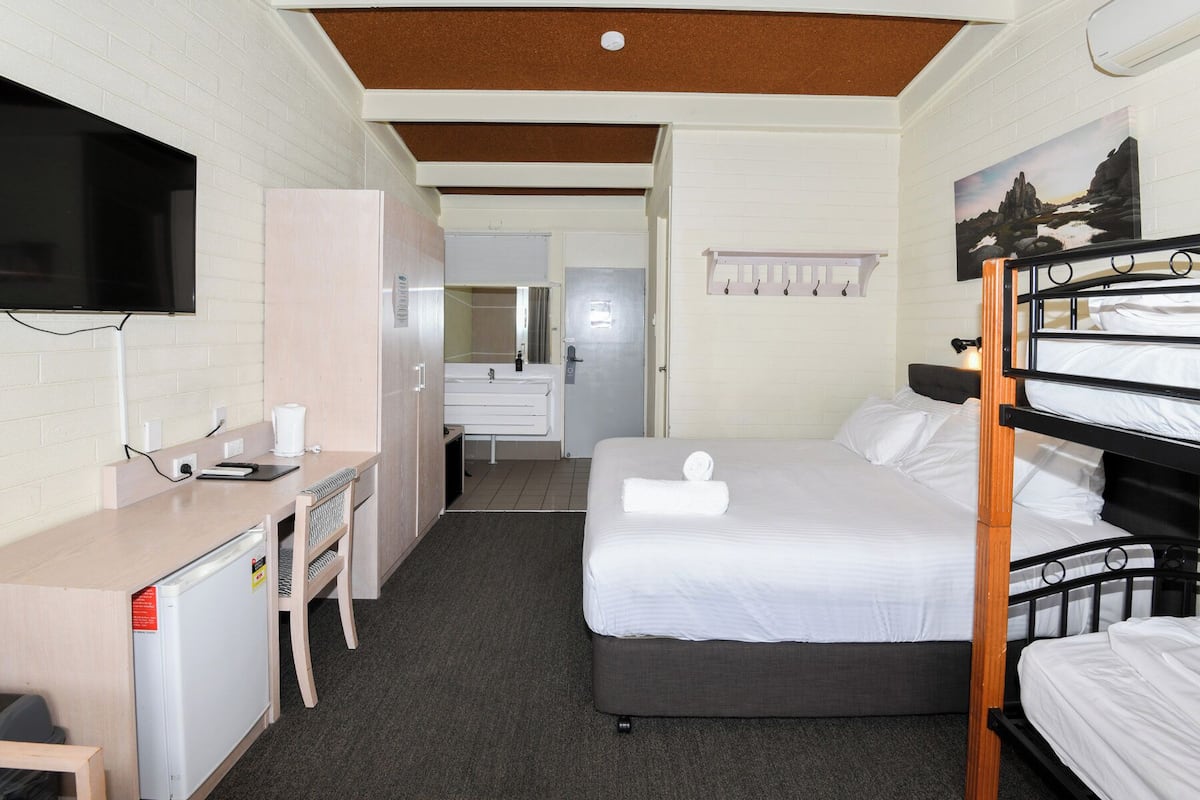 Une chambre d’hôtel compacte avec un lit superposé, un bureau avec une chaise, une télévision et une salle de bain visible à travers une porte ouverte.