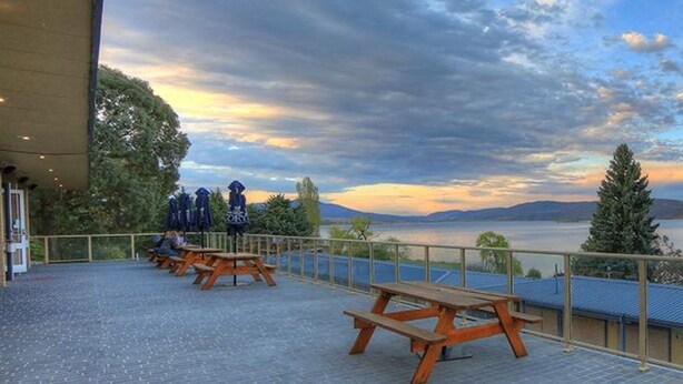 Une terrasse avec des tables de pique-nique offrant une vue sur un lac et des montagnes.