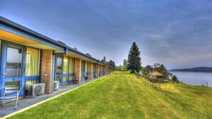 Une rangée de chambres de motel donnant sur une pelouse verdoyante et offrant une vue sur un lac.