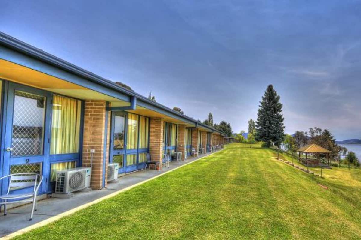 Une rangée de chambres de motel donnant sur une pelouse verdoyante et offrant une vue sur un lac.