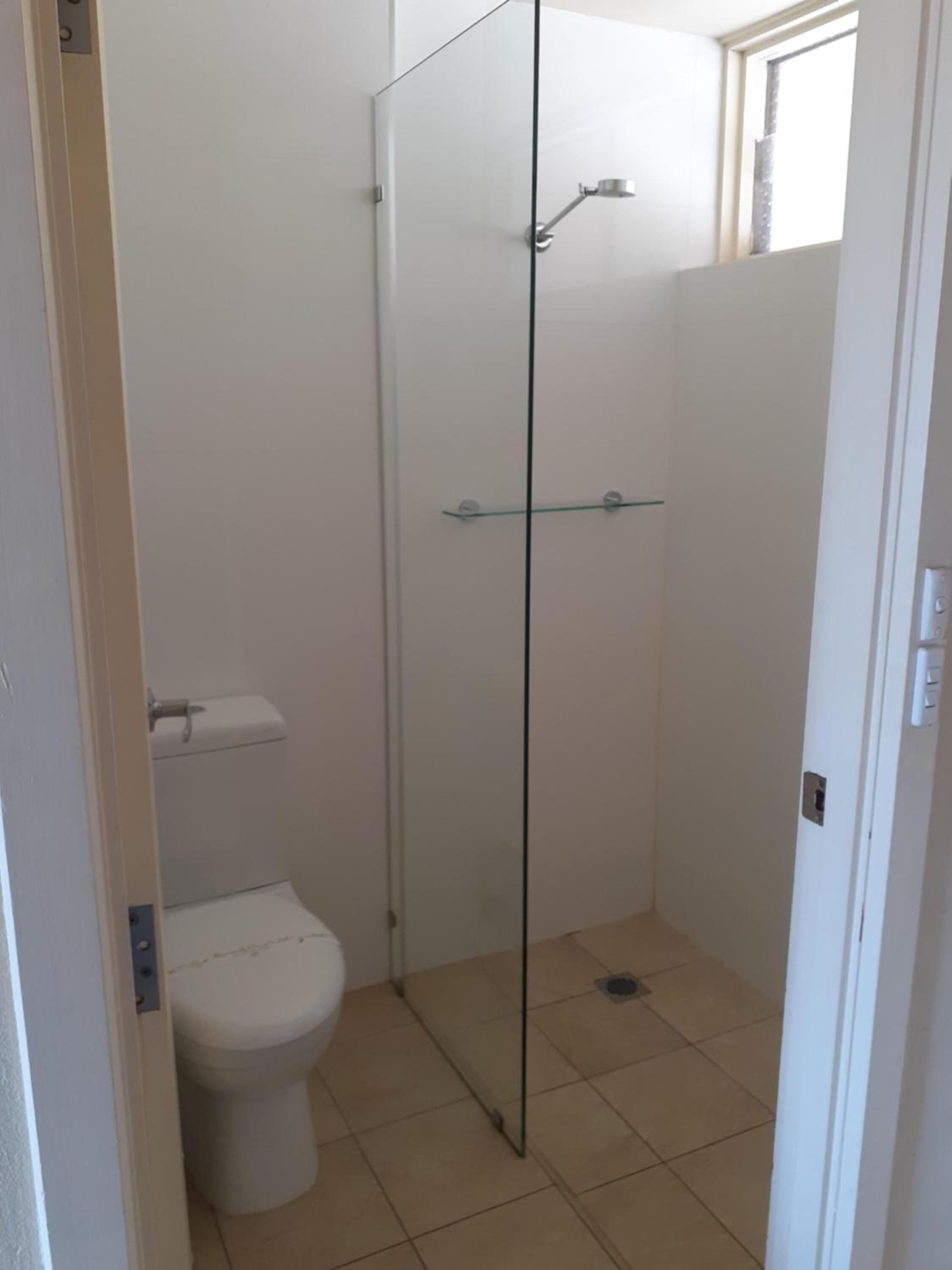 Une petite salle de bain fermée, comprenant des toilettes, une douche en verre et une fenêtre.