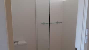 Une petite salle de bain fermée, comprenant des toilettes, une douche en verre et une fenêtre.