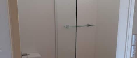 Une petite salle de bain fermée, comprenant des toilettes, une douche en verre et une fenêtre.