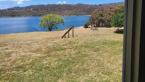 Une vue sur un lac, avec une zone herbeuse et des tables de pique-nique, le tout entouré d’arbres et de collines.