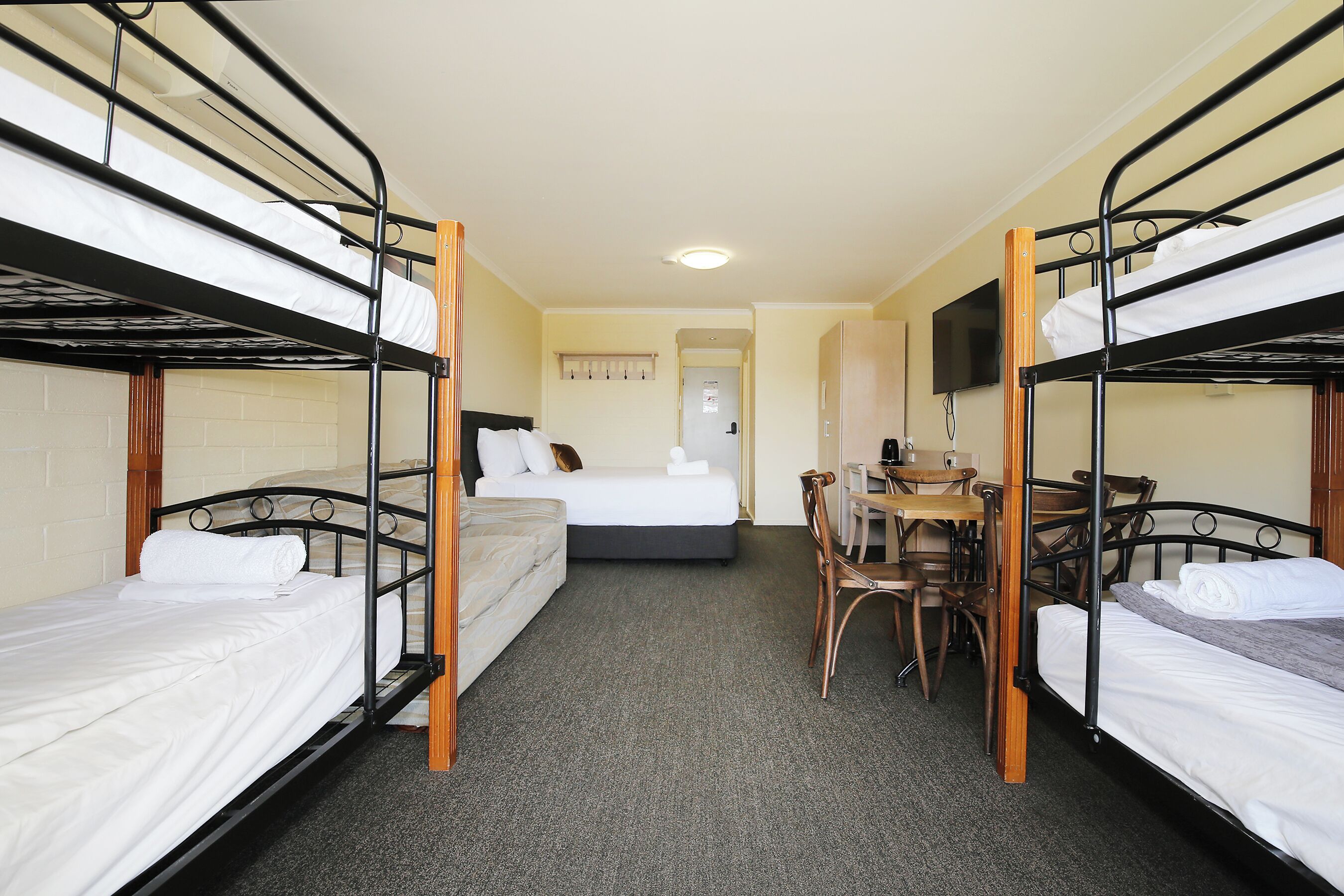 A room with bunk beds, a single bed, a desk with chairs, and a television on the wall.
