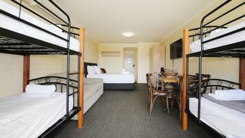 A room with bunk beds, a single bed, a desk with chairs, and a television on the wall.