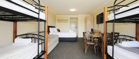 A room with bunk beds, a single bed, a desk with chairs, and a television on the wall.