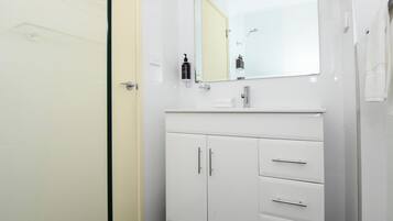 A modern bathroom with a white vanity, a mirror, and a shower area.