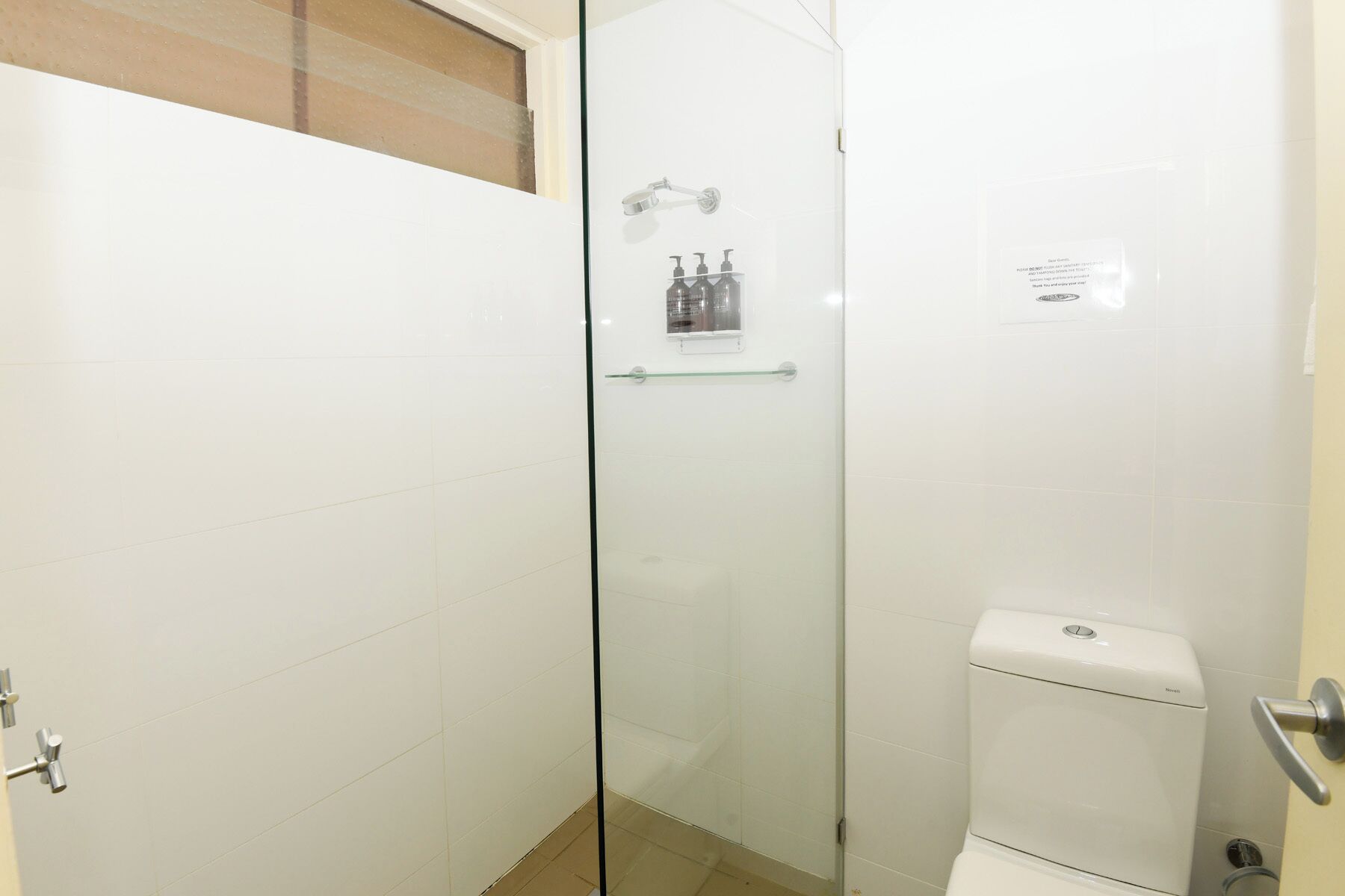 A bathroom with a glass-enclosed shower, a toilet, and a glass shelf with toiletries.