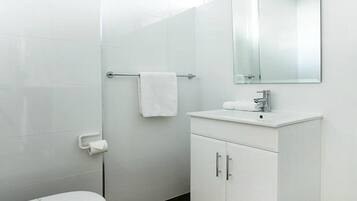 A modern bathroom with white fixtures, a toilet, a sink with a mirror, and a towel rack.