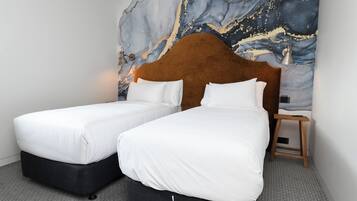 A hotel room with two single beds, a marble wall mural, a wooden nightstand, and a small table.