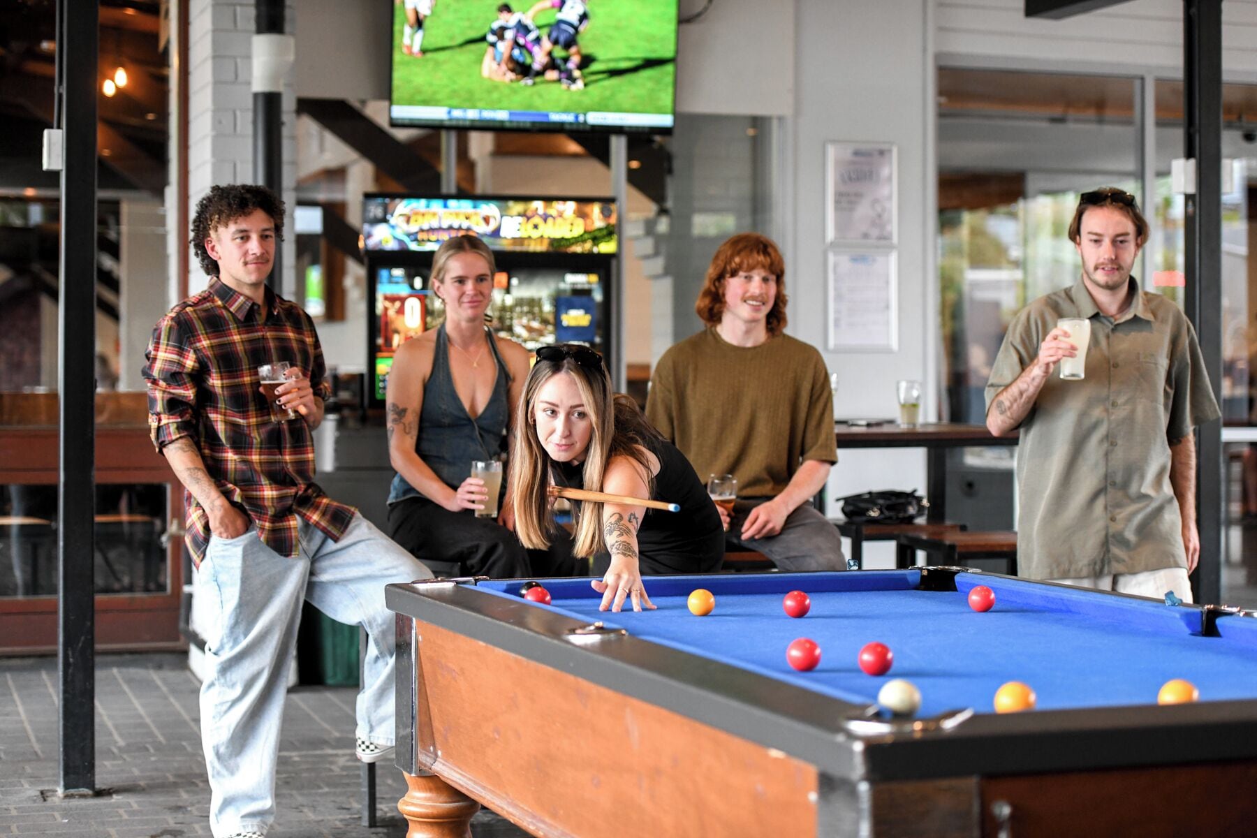 Ein Billardtisch mit Kugeln, ein Fernseher zeigt ein Sportspiel und im Hintergrund eine Bar.