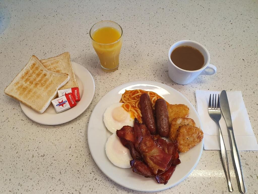 A breakfast plate with toast, eggs, sausages, bacon, and a glass of orange juice.