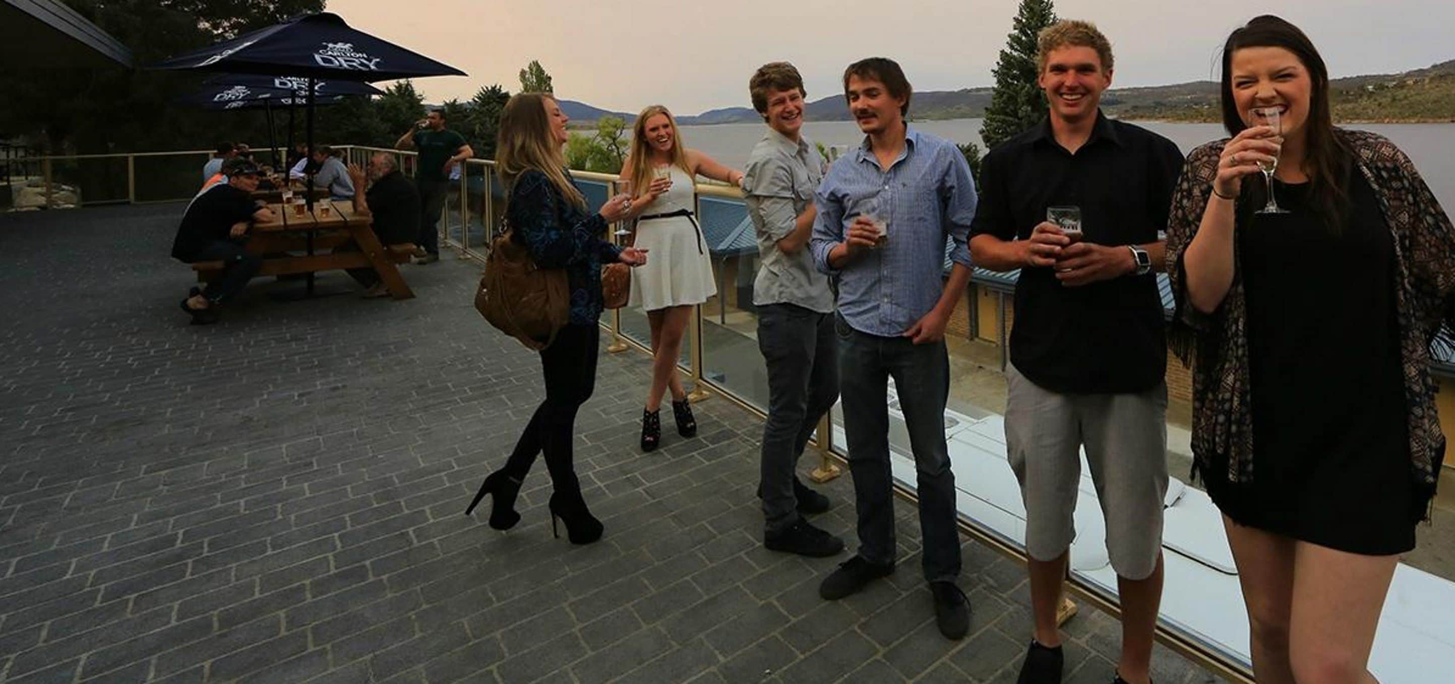 Un grupo de personas en una terraza, con vistas al agua y colinas al fondo.