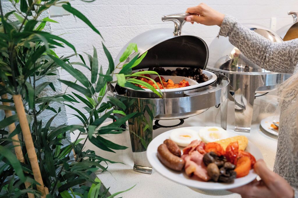 A person serving food from a grill, with a plate of food in hand.