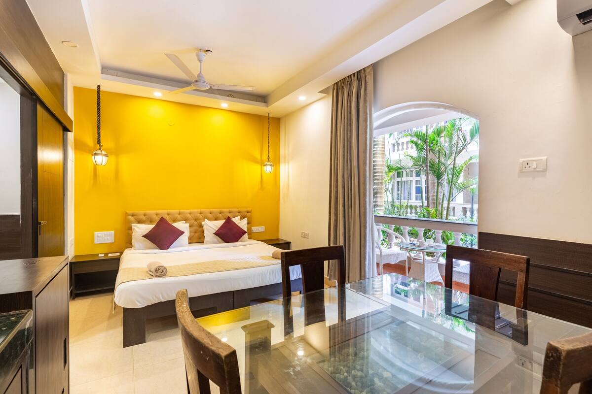 A hotel room with a bed, a glass table, and a view of palm trees.