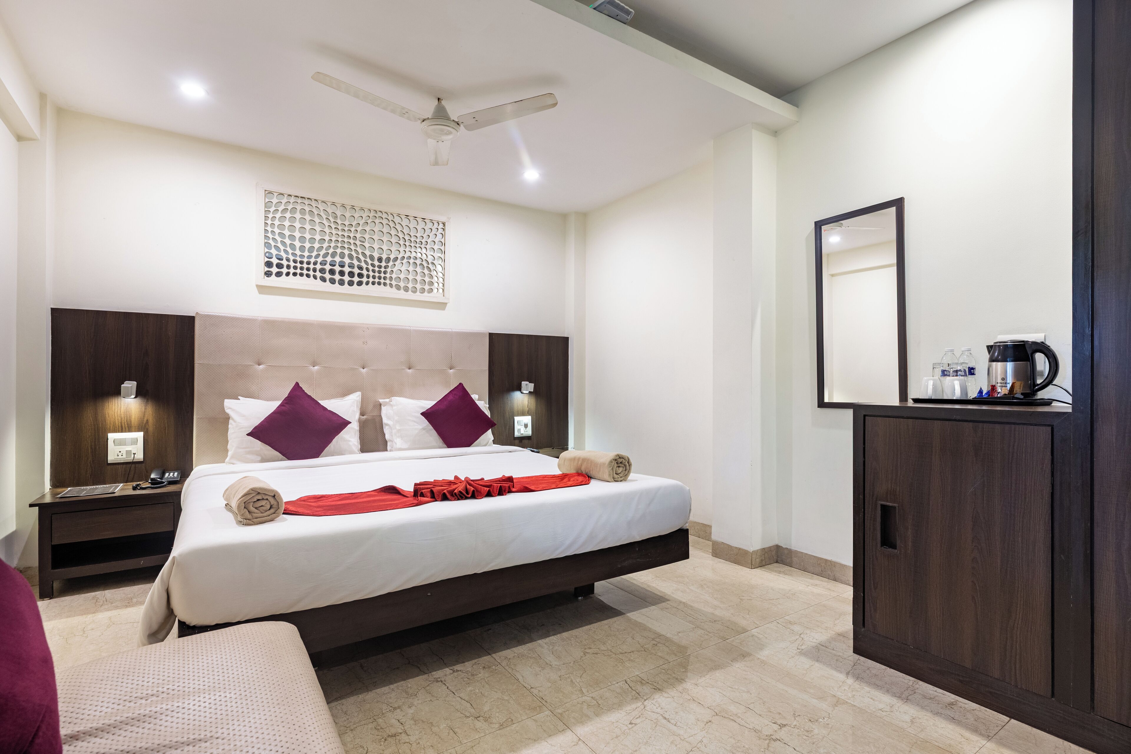 A modern hotel room with a large bed, a nightstand, a wardrobe, and a ceiling fan.
