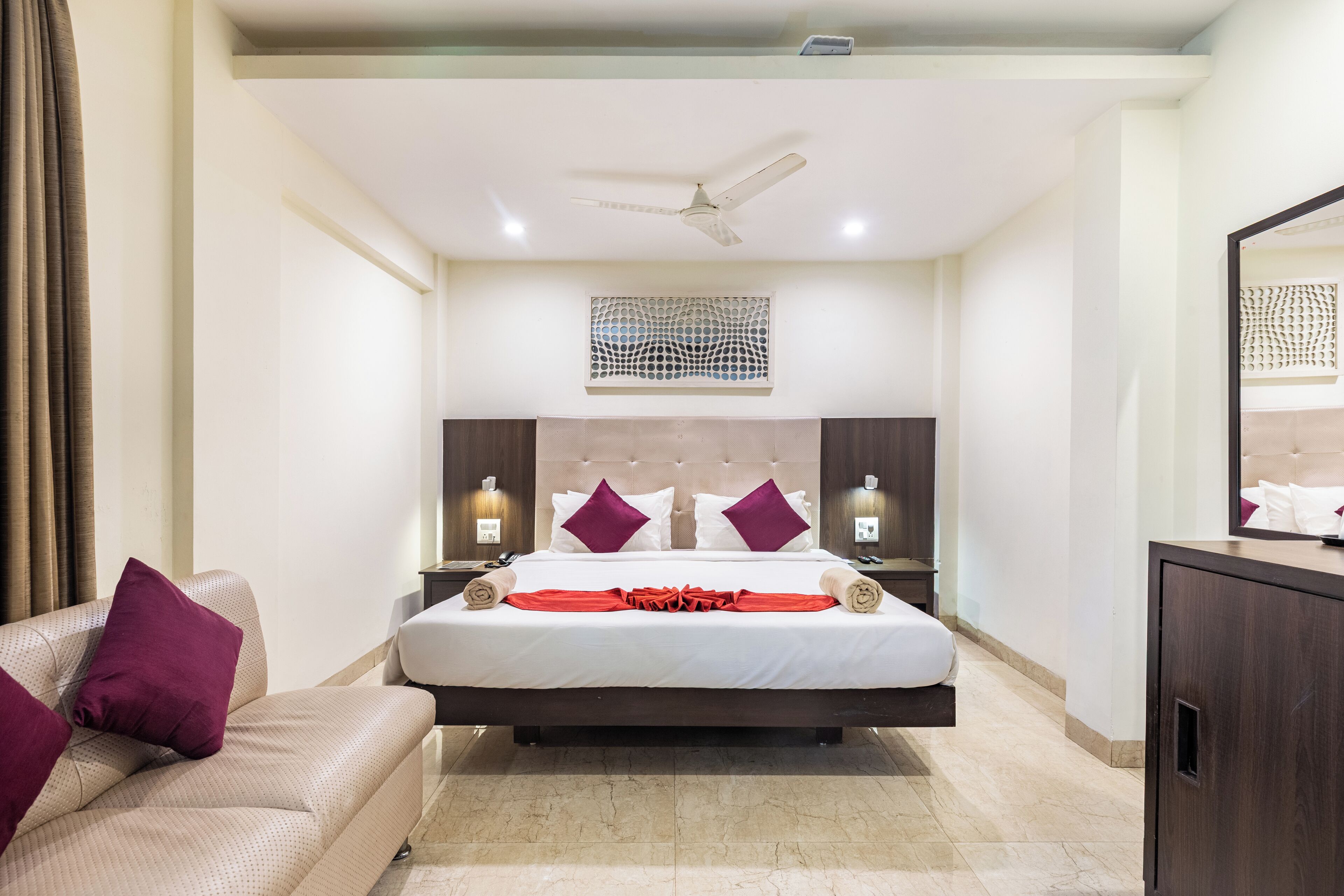 A modern hotel room with a large bed, a ceiling fan, and a decorative wall panel.
