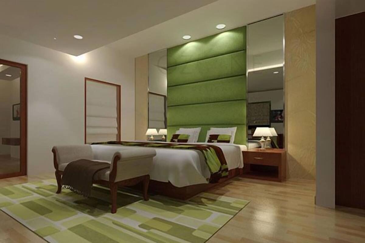 A modern bedroom with a large bed, bedside tables, a mirror, and a green accent wall.