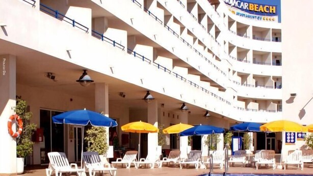 Een hotel met een zwembad, meerdere balkons en buiten zitplaatsen met parasols.