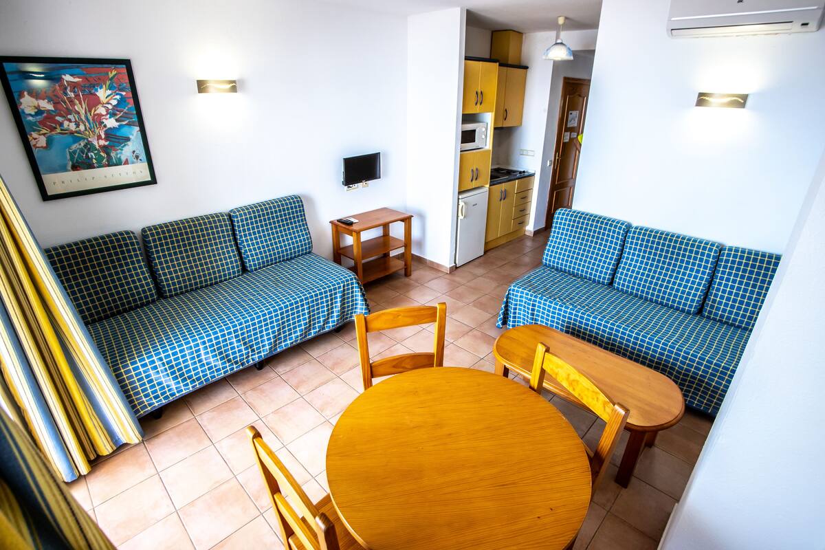 Un espacio habitable compacto con sofá, mesa de comedor y kitchenette.