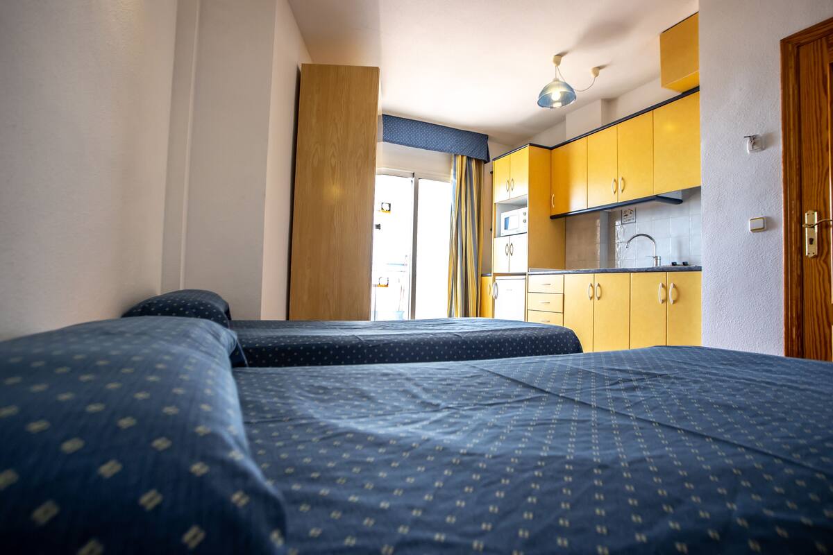 Una habitación con dos camas, un kitchenette y una puerta que da a un espacio exterior.