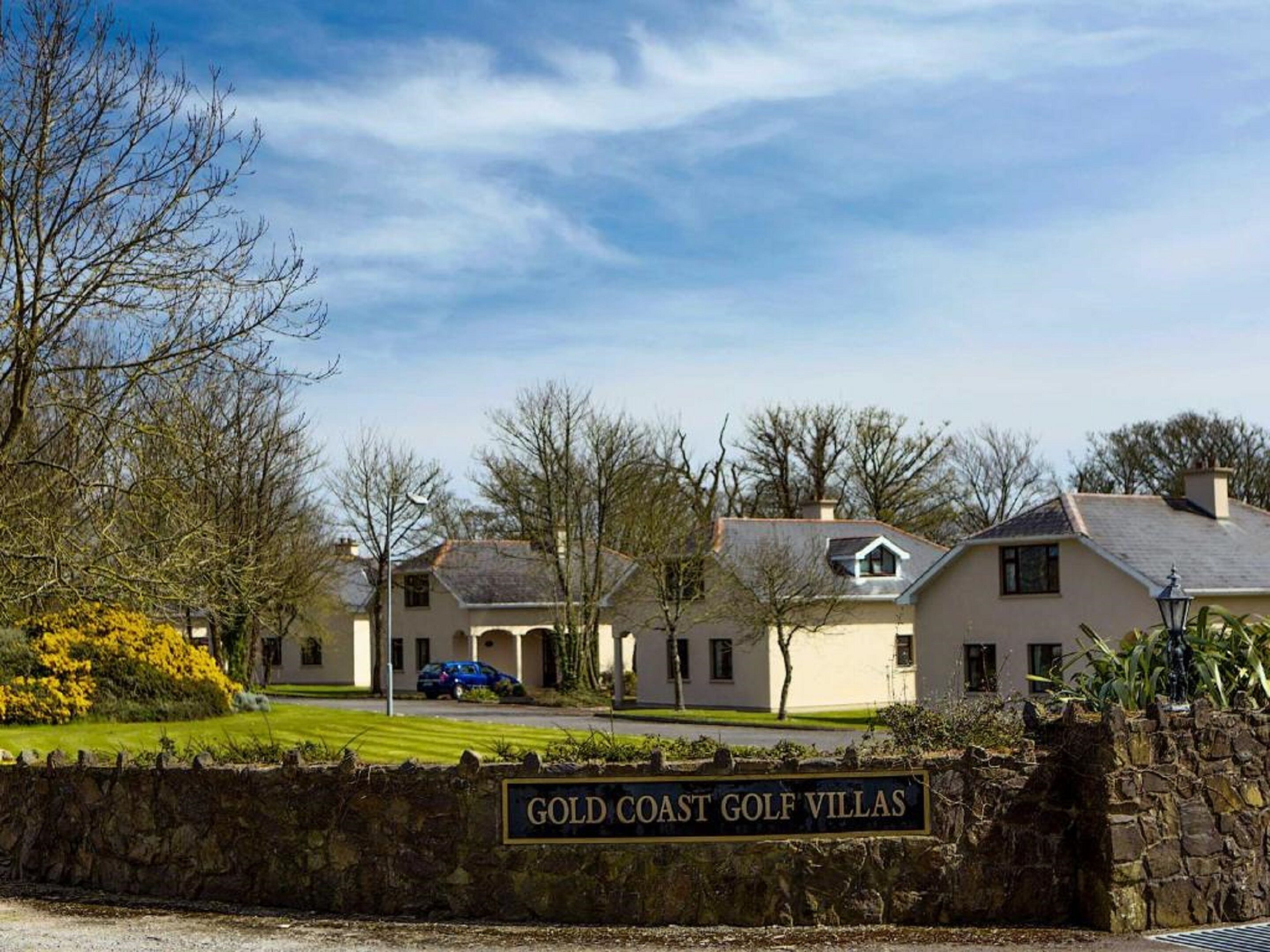 A sign for 'Gold Coast Golf Villas' with a stone wall and a clear sky.
