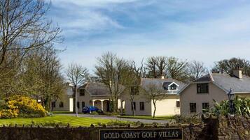 A sign for 'Gold Coast Golf Villas' with a stone wall and a clear sky.