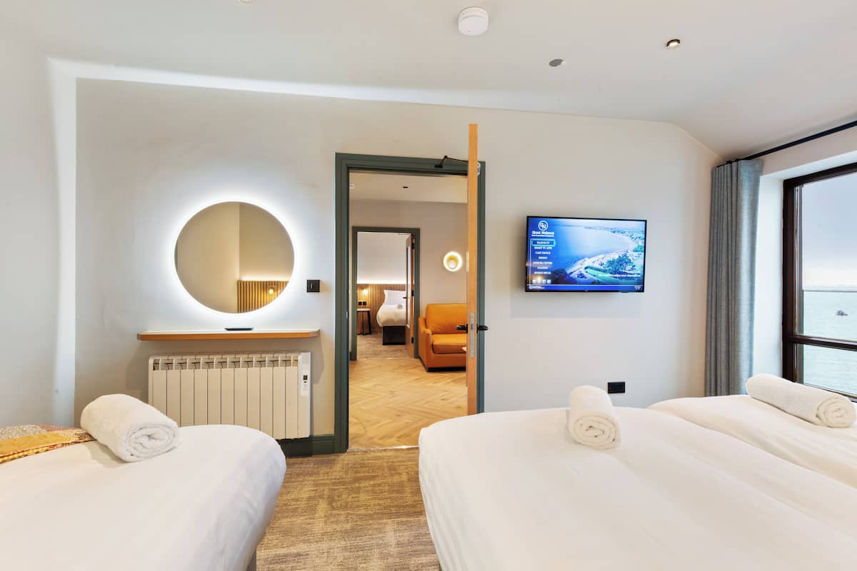 Une chambre d’hôtel avec deux lits, une télévision, une grande fenêtre et une vue sur la mer.