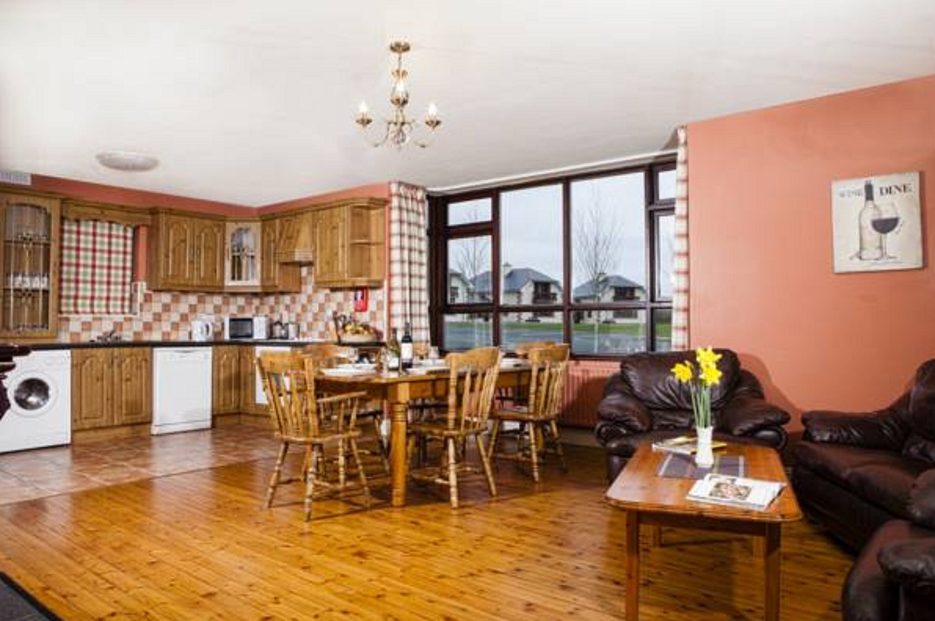 A kitchen with wooden cabinets, a dining table with chairs, a coffee machine, and a washing machine.