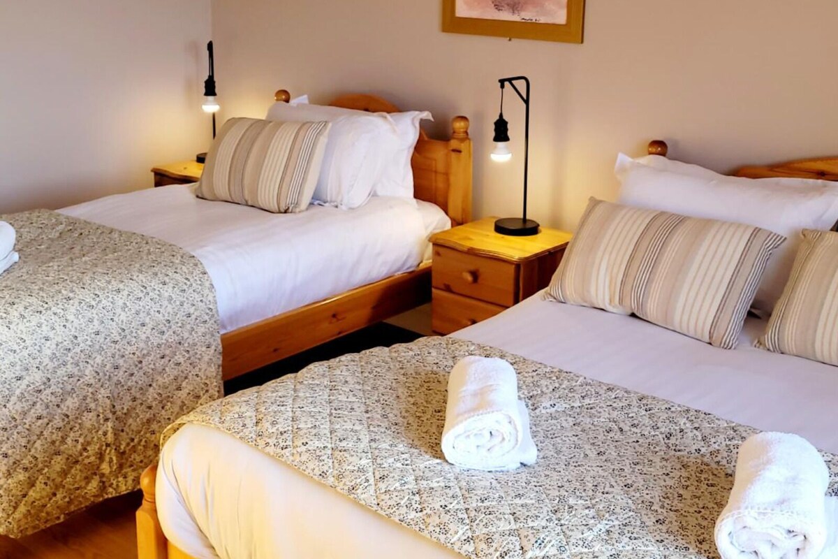 A hotel room with two beds, each with a pillow and a nightstand with a lamp.