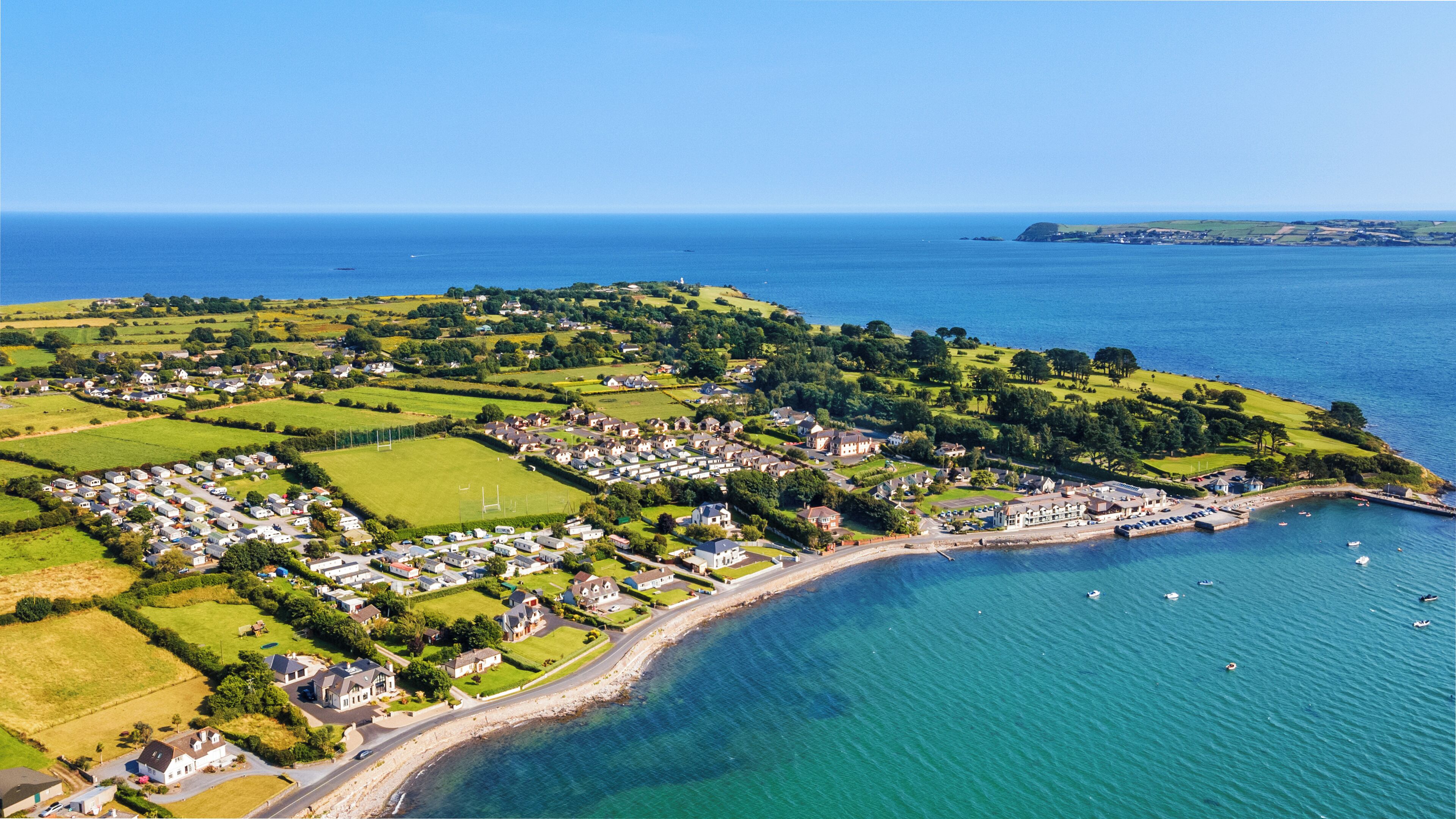 An aerial view of a coastal town with residential areas, green fields, and a marina.